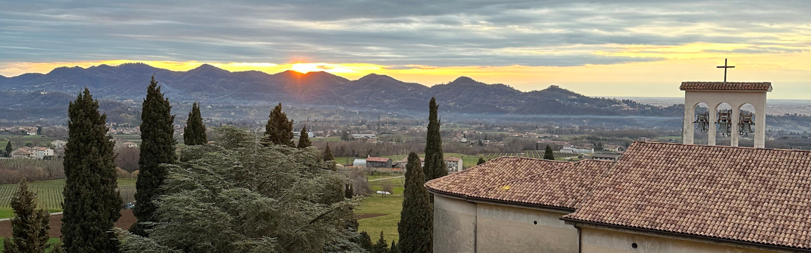 The sun peaking over mountains in the background, while a church with a red tiled roof is visible in the foreground. 